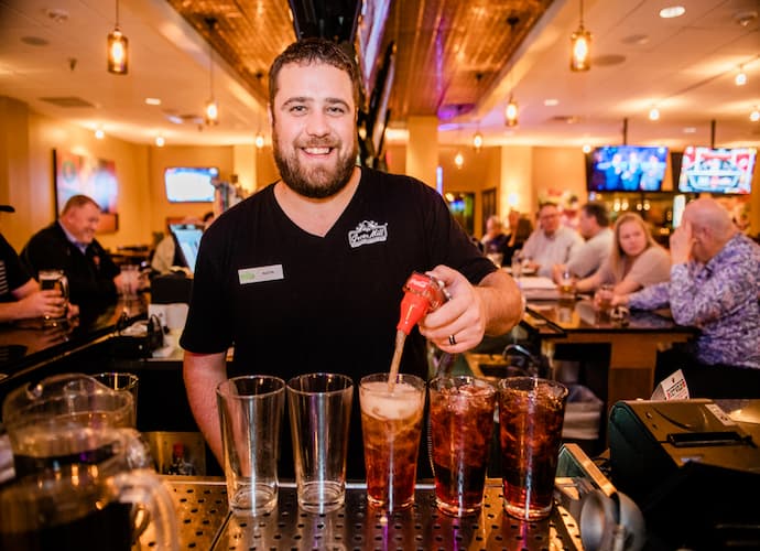 A bar tender at Green Mill Restaurant & Bar pours glasses of soda for rewards club members